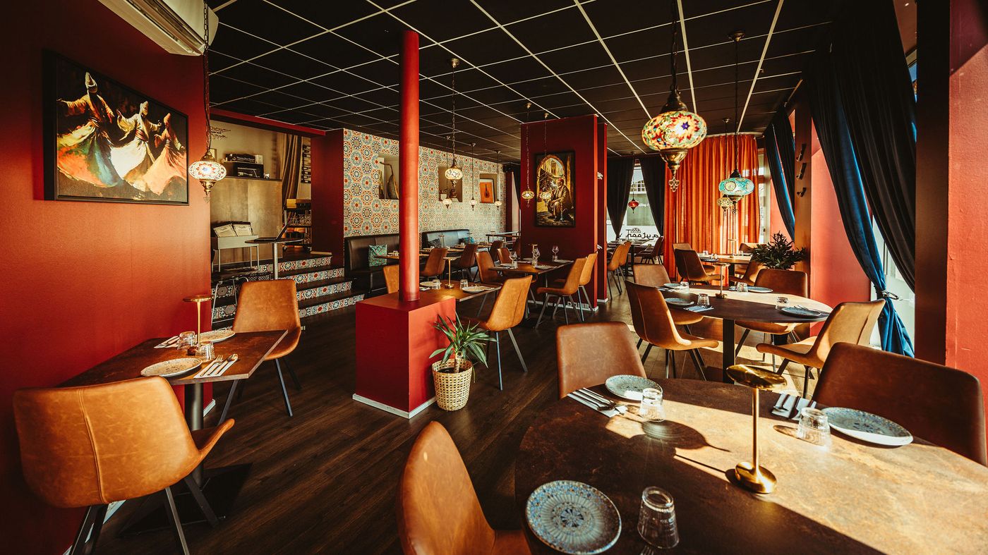 Restaurantens spisestue set i bredformat med flisebelagt trappe, mosaiklamper og et vindue med restaurantens eget spejlvendte skilt.