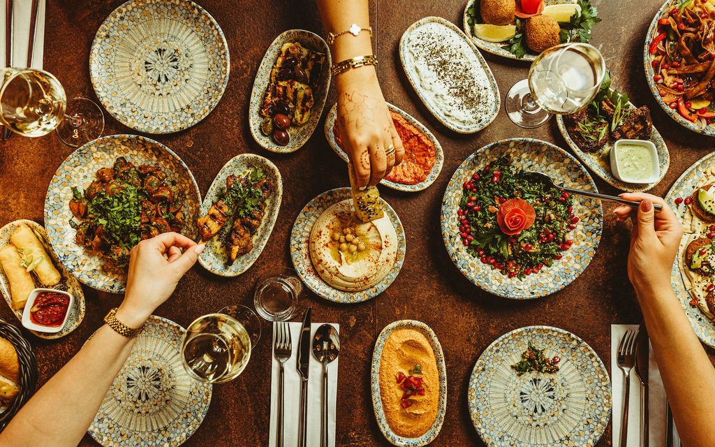Hænder der deler mezze-retter over et fyldt bord, set ovenfra.