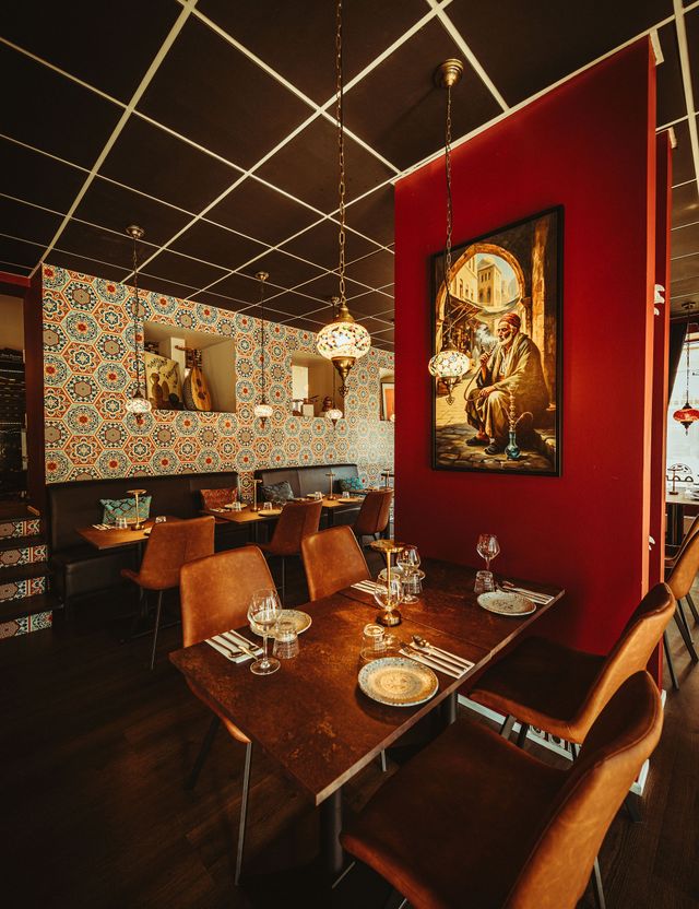 Udsigt gennem restaurantens spisestue med en sekskantet flisevæg, en oud i en niche, et malet portræt og mosaiklamper i loftet.